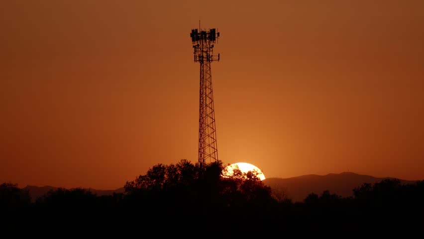 Sunset behind communication tower with birds flying in sky 