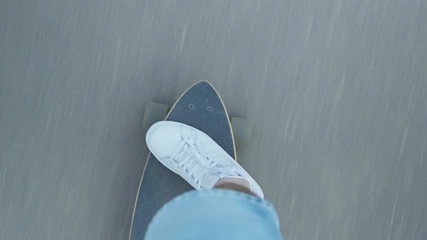 Young male skateboarder on city street. Man in white sneakers rides longboard on asphalt. Man ride skateboard. Top view handheld shot. Close-up in 4K, UHD
