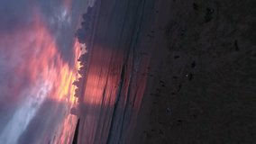 Vertical video. Scarlet clouds sunset exotic island sea ocean with surfer on surfboard at calm water surface aerial view. FPV sport drone low shot people relaxing surfing extreme hobby activity sky 4k