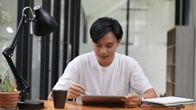 Positive asian guy using tablet for online communication, scrolling news feed, messaging in social media, Man holds tablet and smiling enjoy new mobile application on couch in living room at home - Powered by Shutterstock - Get 15% off with code: PIKWIZARD15