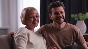 Adult man having fun with his mother. An adult son and his mother are sitting on the sofa in the living room and laughing. - Powered by Shutterstock - Get 15% off with code: PIKWIZARD15