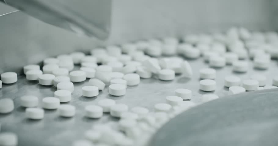 White pills moving on metal automatic line in workshop of pharmaceutical factory. Process of production of pills, drugs. Factory equipment and machine conveyor. Industrial pharmaceutical concept.