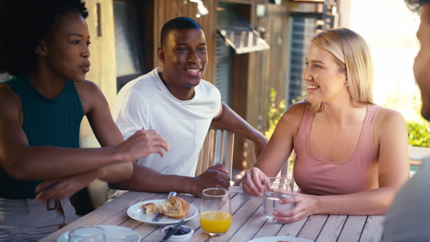 Smiling group of smiling friends on holiday eating breakfast outdoors together looking at mobile phone - shot in slow motion Royalty-Free Stock Footage #1104190317
