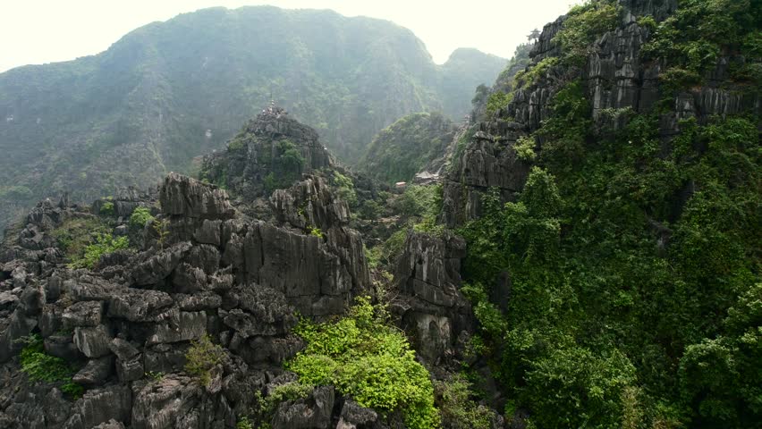 Mua Cave Viewpoint in Ninh Binh Vietnam. Close view of striking limestone cliffs, Flying in mountains valley revealing tourists climbing stairs towards an ancient temple on the peak Royalty-Free Stock Footage #1104191031