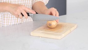 A woman is peeling onions on a board at the table. The cooking process.