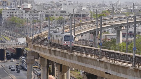 A metro train is passing on a bridge on the subway track with the busy road with vehicles and urban Indian city landscape or buildings in the background, Jaipur, Rajasthan, India  Arkivvideo