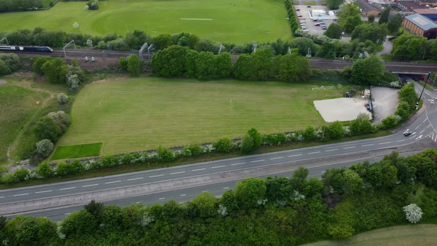 Drone footage showing town bypass roundabout and passsenger train running alongside with high school in the background, Wilmslow, Cheshire, England, UK, Europe