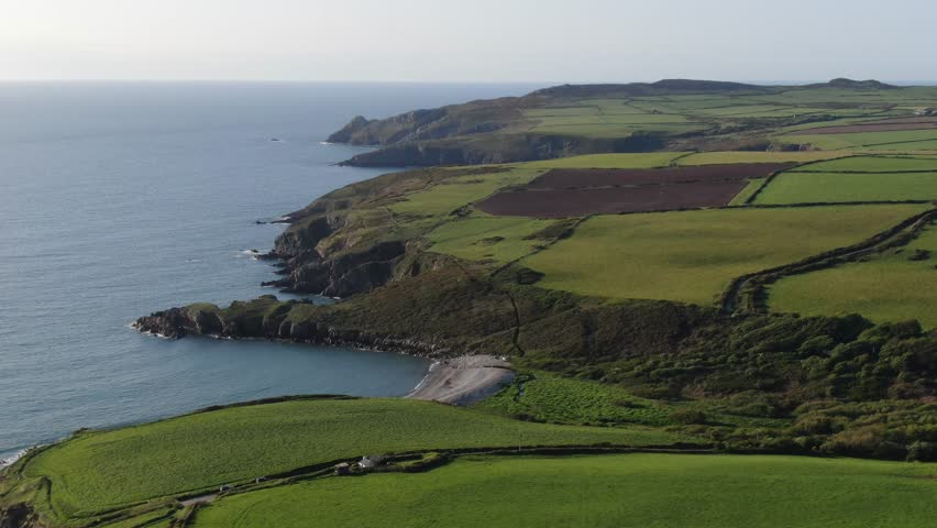 Wide dramatic landscape drone shot of beautiful scenic Welsh coastline shore in Pembrokeshire Coast National Park with cliff sea beach bay island rocks fields on blue sky sunny summer day