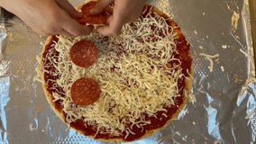 A young boy that is putting pepperoni slices on a homemade pizza.