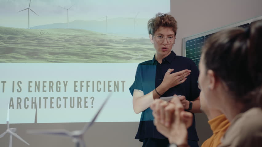 Young female engineer explaining presentation about energy efficient architecture on projection screen and talking to colleagues on office meeting, working in green energy company