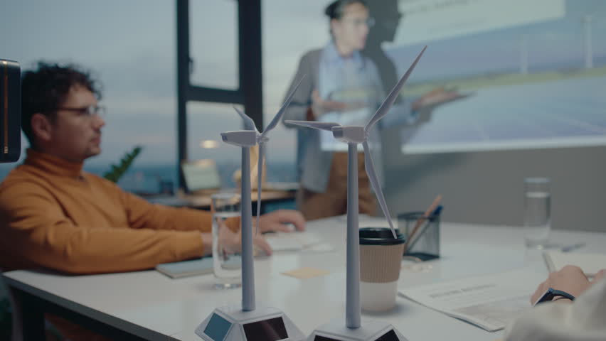 Wind turbine models on meeting table in the office of eco-friendly company, colleagues discussing presentation in the background. Close-up shot Royalty-Free Stock Footage #1104197979