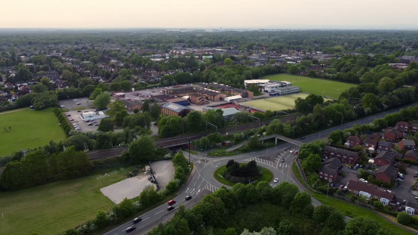 Drone footage showing town bypass and railway running alongside and high school in the background and modern housing estate to the right, Wilmslow, Cheshire, England, UK, Europe