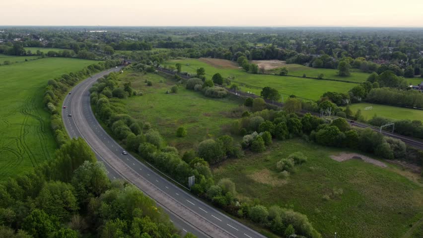 Drone footage showing town bypass and train running alongside and crossing the road in the distance, Wilmslow, Cheshire, England, UK, Europe