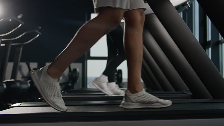 Side view legs in sneakers walk on treadmill in fitness gym unknown woman and man going footstep sport people runners walk on running machine slow stride foot step pace cardio workout health lifestyle Royalty-Free Stock Footage #1104200449