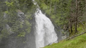 slow motion video of a waterfall in a beautiful mountain forest with conifers, the views of the dolomites and the silk effect of the waterfall

