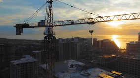 New modern apartment buildings, high-rise building with construction crane against backdrop of sunset, sun on ocean or sea. Drone view of crane construction site over city at sunset. Contractor. - Powered by Shutterstock - Get 15% off with code: PIKWIZARD15