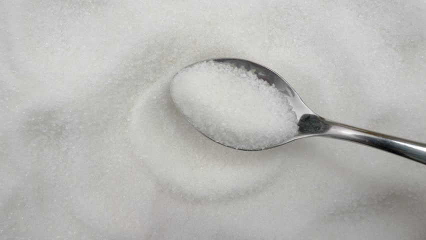 Sugar. Putting white granulated sugar in a teaspoon, view from top.