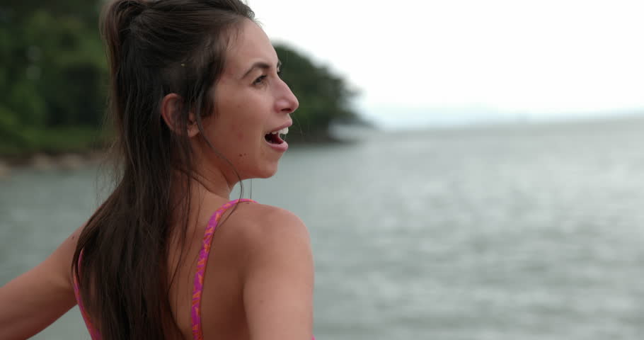 Woman stands on beach overlooking ocean in morning yawns - side profile
