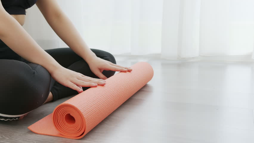 Close up of young woman dressed in yoga sportswear rolling out an orange yoga mat indoors, fitness and recreation concept. Royalty-Free Stock Footage #1104204977