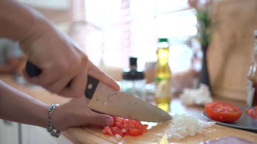 Unrecognizable man using a kitchen knife to chop or slice a tomato and onion in the kitchen, man preparing an ingredients for cooking. Man chopping tomato and onion close up.