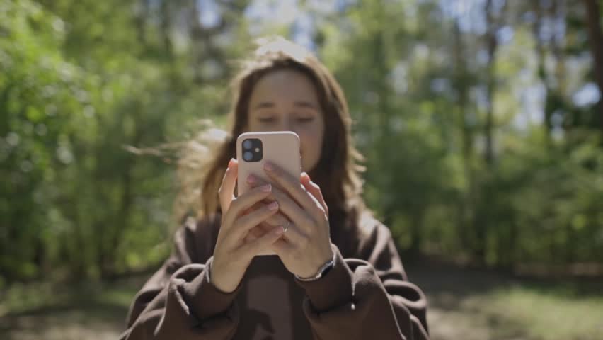Сaucasian girl photographs a beautiful landscape in a sunny park close-up. girl walks in the park and shoots on a mobile phone. the girl holds a smartphone in front of her and takes pictures of nature