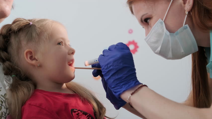 A pediatrician in a hospital examines the oral cavity and throat of a little girl. | Shutterstock HD Video #1104209613