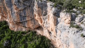 Panoramic beautiful vertiginous aerial view of wooden staircase at rock cliff as part of hiking path in Congost de Montrebei gorge surrounded by vegetation on river in Catalonia, Pyrenees, Spain. 4K .