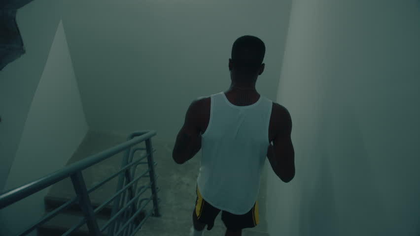 Black basketball player in sportswear carrying ball walking downstairs in apartment building. High angle shot