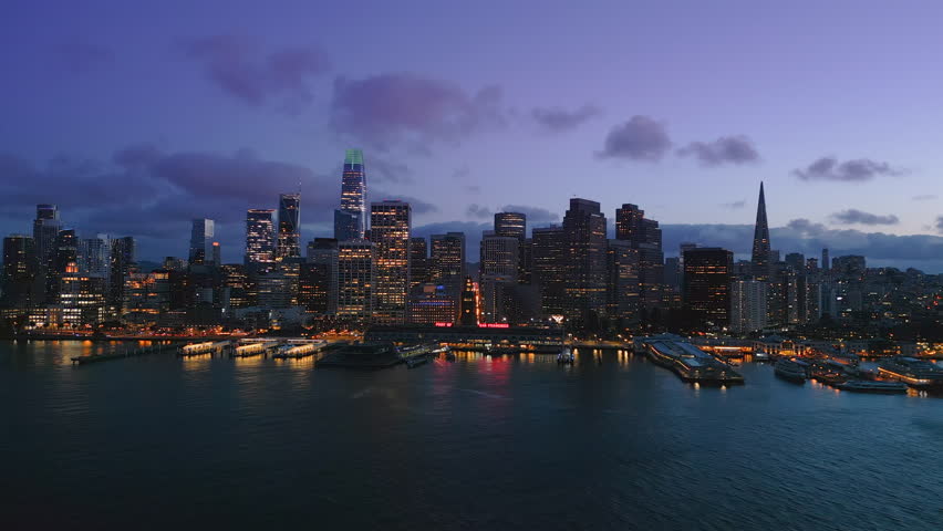 Amazing Arial view Of The San Francisco City Skyline and Ferry Terminal during gorgeous sunset time. Purple sky and clouds behind the nighttime skyscrapers. SF, California. USA Royalty-Free Stock Footage #1104212613
