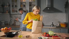 Slow motion. Caucasian young happy emotional loving couple unpacking disposable paper bag with groceries in the cozy home kitchen., standing by kitchen island with organic vegetables and fruits. - Powered by Shutterstock - Get 15% off with code: PIKWIZARD15