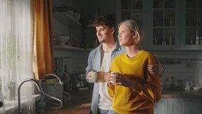 Beautiful affectionate happy couple hugging, enjoying new morning day together, standing by kitchen window and drink aroma coffee. Lovely woman and handsome man enjoy closeness. Family relationships - Powered by Shutterstock - Get 15% off with code: PIKWIZARD15