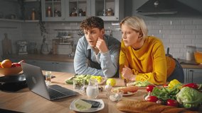 Young couple in love watches online video lesson or tutorial cooking class on laptop, learning new recipe together, checking ingredients on countertop, enjoying preparing meal together in home kitchen