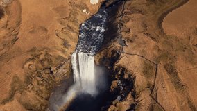 Drone shot of skgafoss waterfall forming beautiful rainbow, icelandic landscape with nordic nature. Spectacular scandinavian cascade flowing down off of cliffs, panoramic view. 60 fps video.