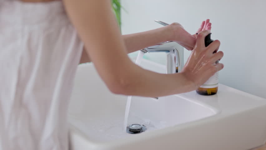 Washing hands, clean and soap and water for hygiene, germ protection and safety. Sanitary, healthy and a woman cleaning fingers of bacteria, virus or prevention of sickness in a bathroom sink | Shutterstock HD Video #1104223721