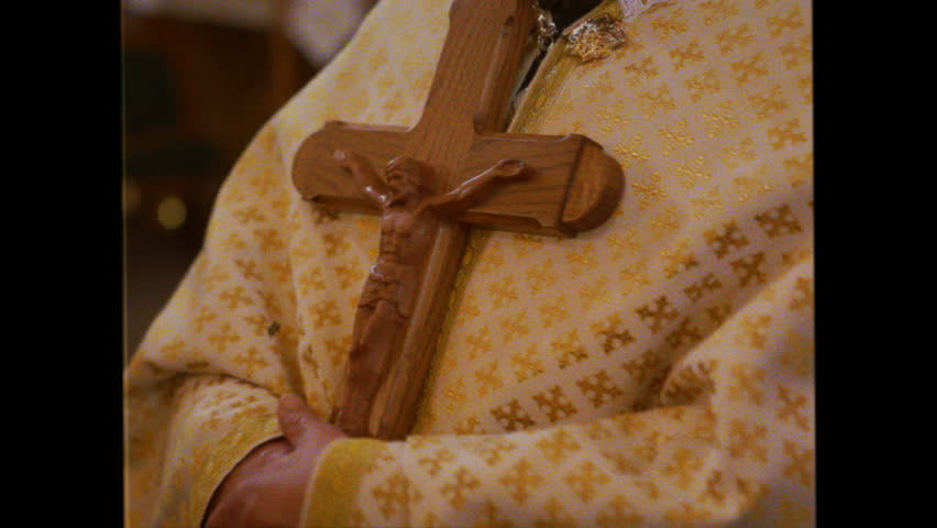 An Orthodox priest in a church holds a large wooden cross in his hands. Old archive video taken with an analog camera, circa 1980.