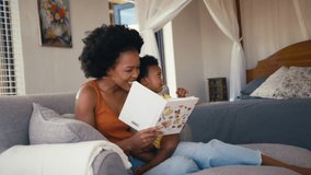 Family sitting on sofa at home with parents reading book with young daughter - shot in slow motion - Powered by Shutterstock - Get 15% off with code: PIKWIZARD15