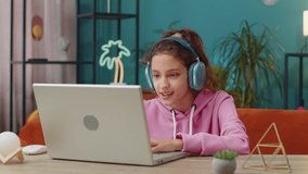Preteen school girl looking at laptop camera, making video webcam conference call with friends or teacher, enjoying pleasant conversation, waving hello hi. Young child, kid at home workplace table