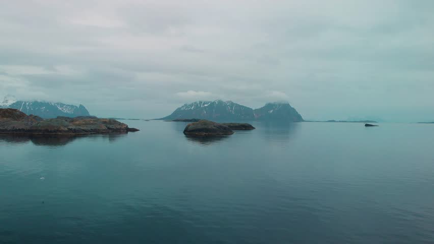 Aerial drone shot of a foggy ocean in Lofoten Norway. With rocks and mountains in the background.