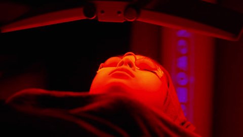 Asian woman getting modern cosmetology facial red LED Light Therapy at beauty clinic. Attractive girl having facial cosmetic skin care treatment for skin rejuvenation, anti-aging and acne at spa salon Arkivvideo