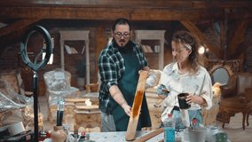 Young male craftsman and woman recording video on a phone camera to show how to work and take paint on wood plank in an antique workshop. Personal channel or blog online and distant learning - Powered by Shutterstock - Get 15% off with code: PIKWIZARD15