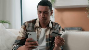 African American man frustrated confused guy at home couch problem with online payment with phone and credit card bank failure try to pay e-bank app error no money scam fraud unsuccessful transaction - Powered by Shutterstock - Get 15% off with code: PIKWIZARD15