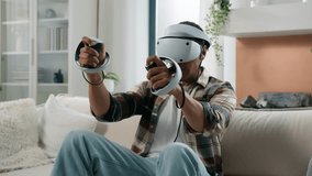 African American man having fun at home couch with virtual reality video game fight guy play 3d cyber gaming fighting with controllers man playing in VR glasses helmet using joysticks metaverse world