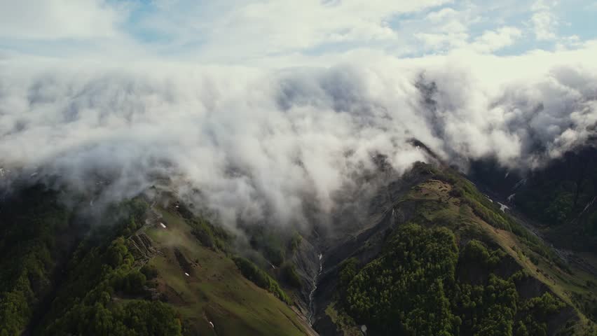 Aerial drone view of heavy fog clouds flowing over the mountain. Foggy clouds hanging in the mountains. Beautiful mountain view of the snow-capped peaks near Gudauri, Georgia.