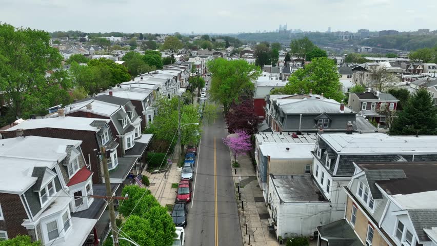 Aerial reverse dolly over street in town in America. Large USA urban skyline in distance. Housing in spring. Reveal of church and American flag on house. Bugs flying near drone.