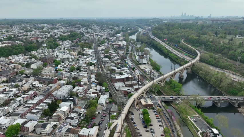 Aerial descending shot of Manayunk Pennsylvania, outskirt of Philadelphia. Iconic bridge and houses on cloudy spring day.