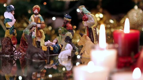 Christmas nativity scene with candles in front of Christmas tree. The focus moves from candles to figurines.