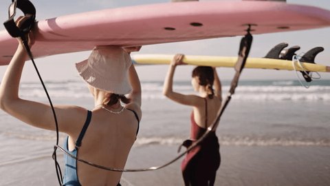Young women carrying surfboards walking talking on ocean beach. Active surfer sports women friends couple getting ready to practice in the sea, catch a wave on a high tide. Stockvideo