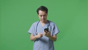 Asian Male Doctor With Stethoscope Waving Hand And Having A Video Call On Smartphone While Standing On Green Screen Background In The Hospital
