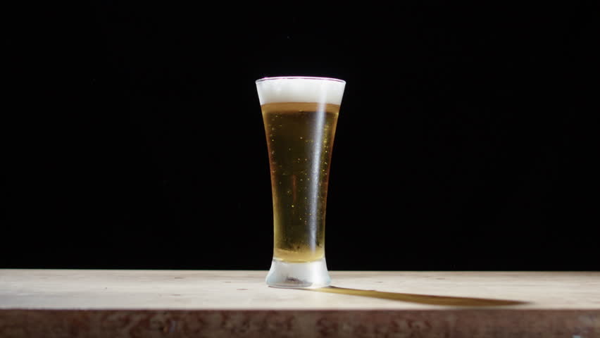 Beer glass smashed with sledge hammer spills beer everywhere, black background Royalty-Free Stock Footage #1104245635