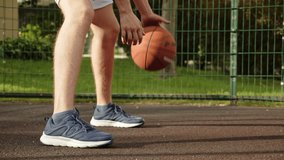 Footage of a teenager dribbling on an outdoor court, during a bright and sunny summer day. Video of a white caucasian teen training to play basketball. Video of a male doing basketball tricks. 